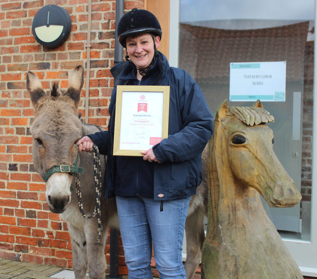member of staff stood holding a donkey and a 'visit england' certificate