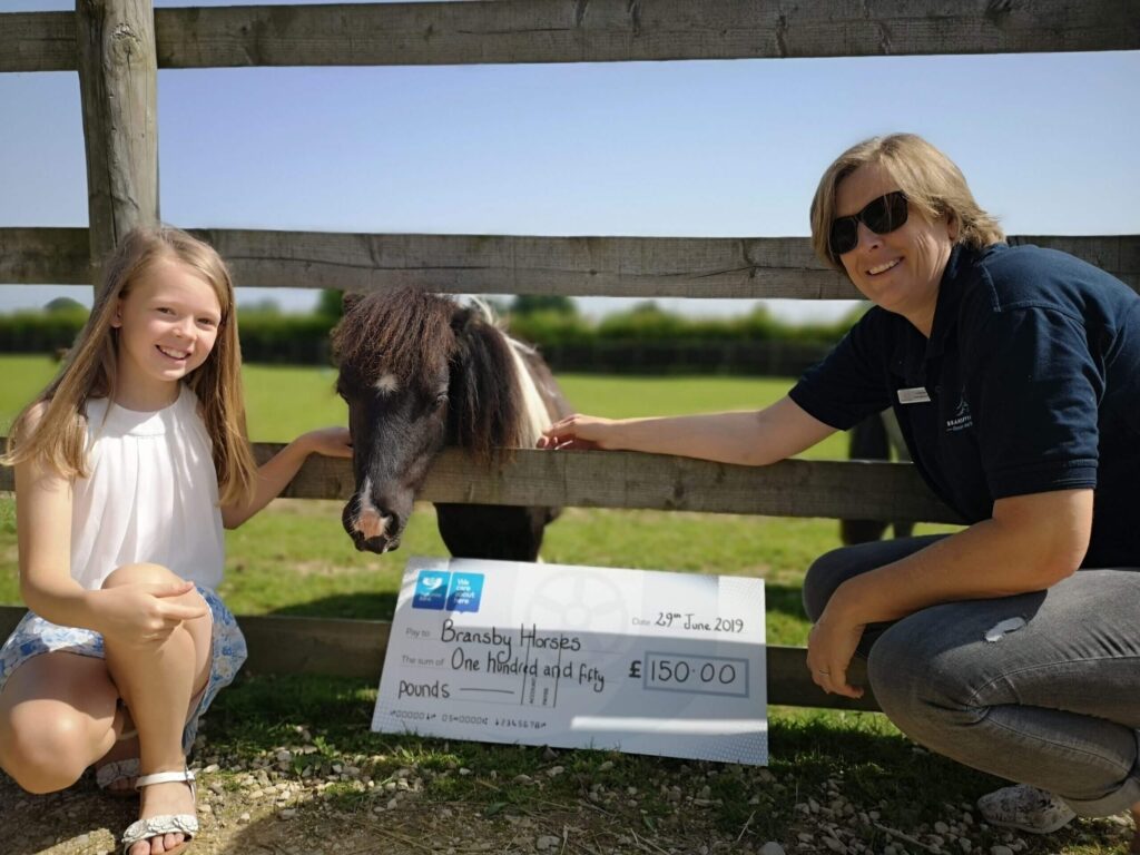 member of staff and a little girl stood in front of a shetland pony with a cheque for 150 pounds in between them