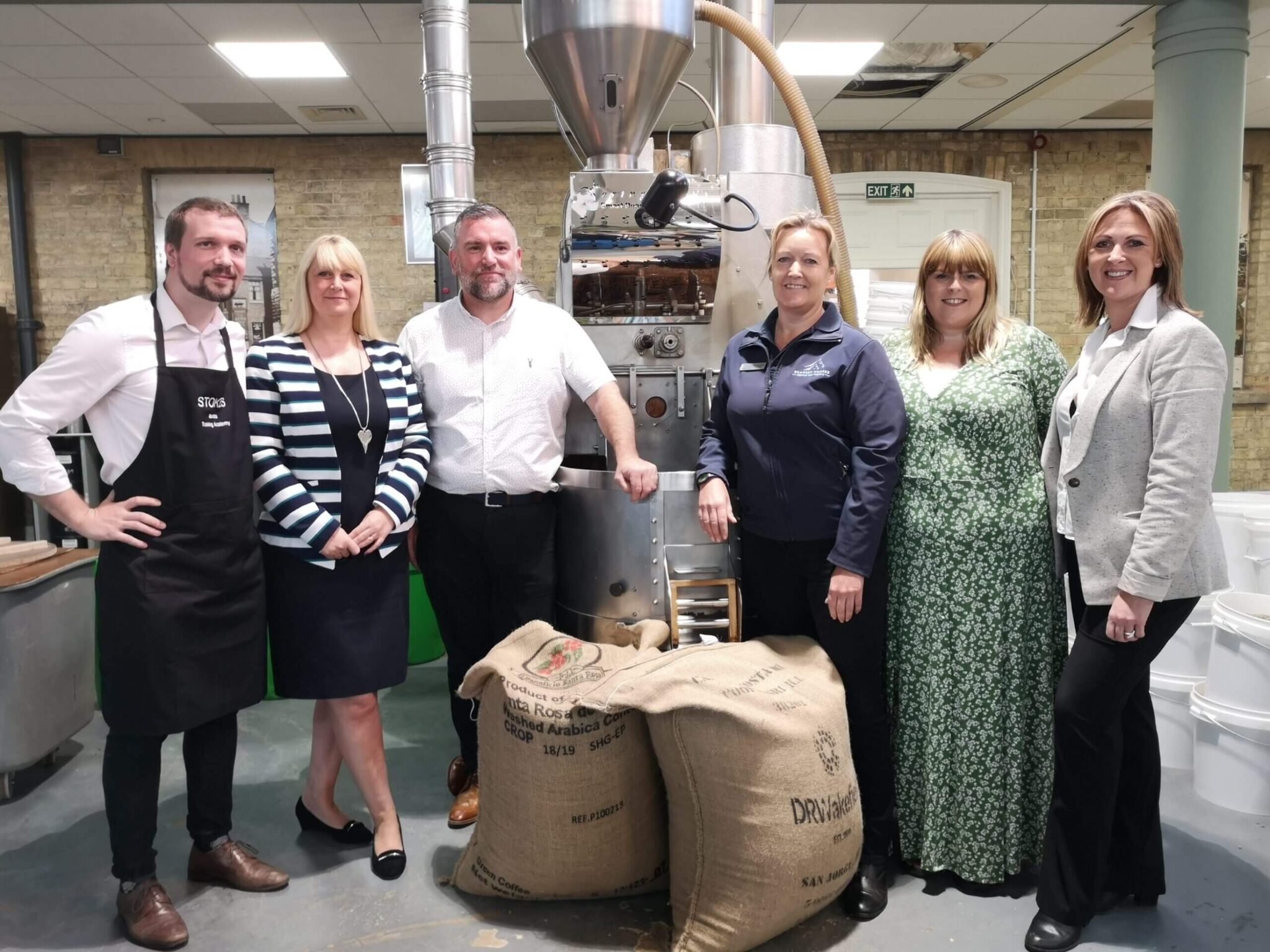 members of staff stood next to stokes coffee employees with bags of coffee beans between them