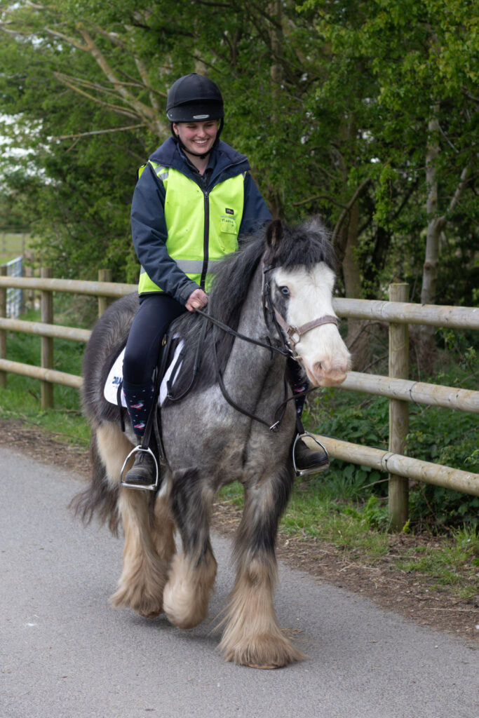 A woman in a reflective jacket riding a grey cob with a white face