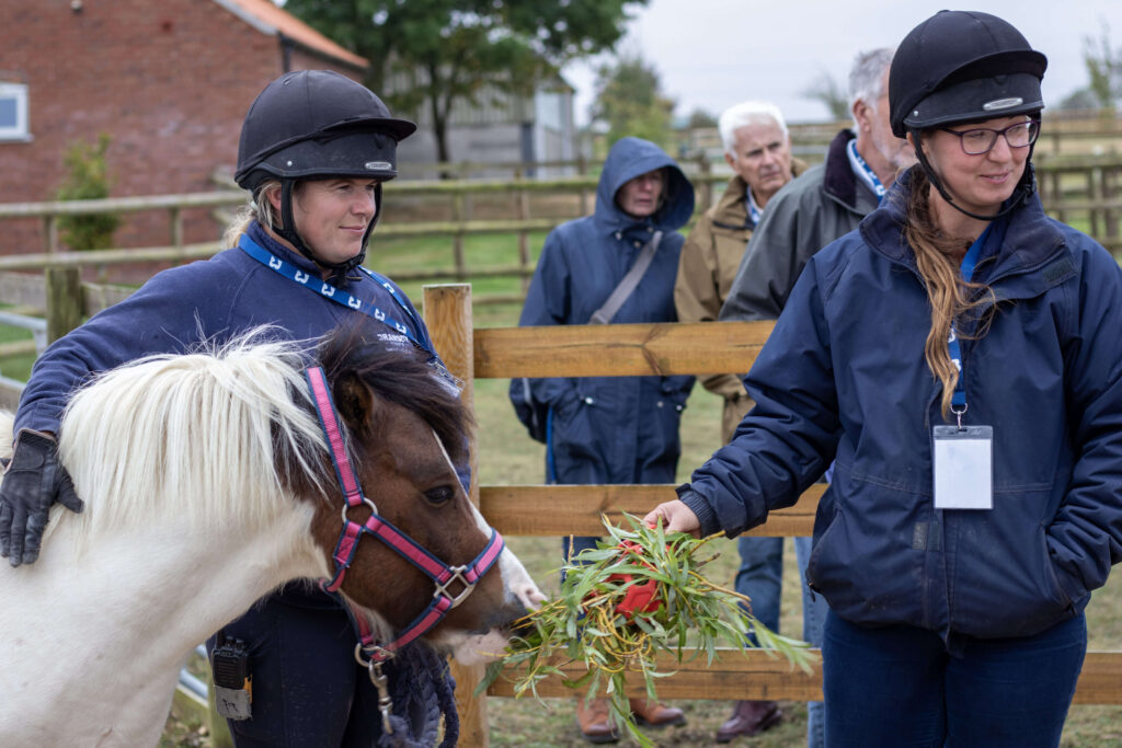 two members of staff stood in front of a group of people with a pony
