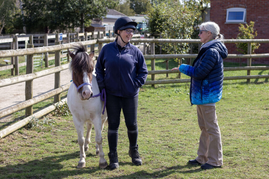 visitor talking to a member of staff with a pony stood beside them