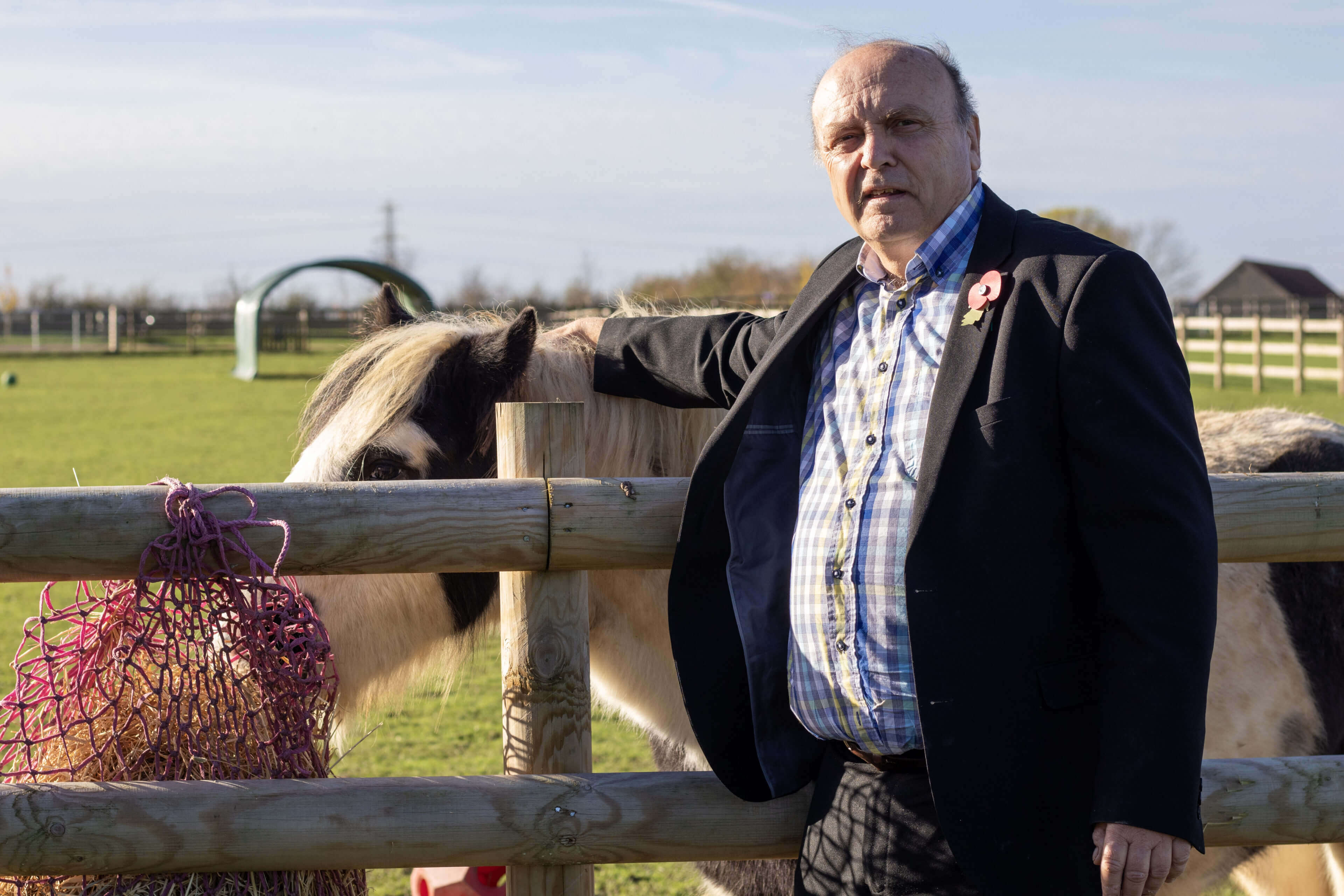 trustee stood in front of a fence with a horse eating out of a haynet behind him